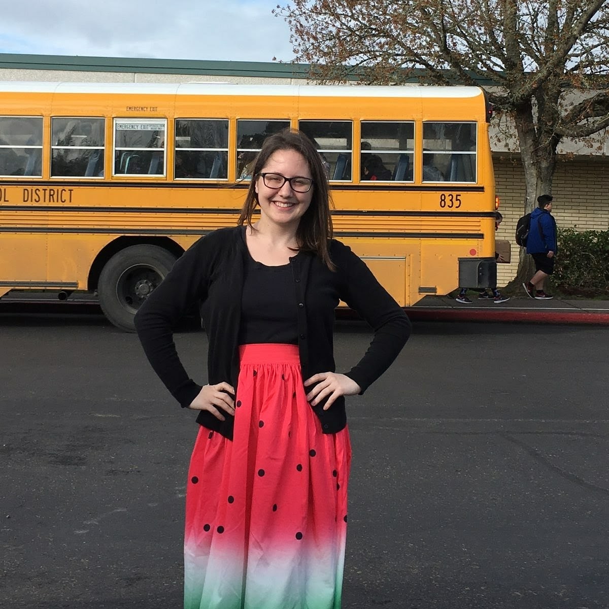 Cindy standing in front of a school bus. She has her hands on her hips and is smiling.